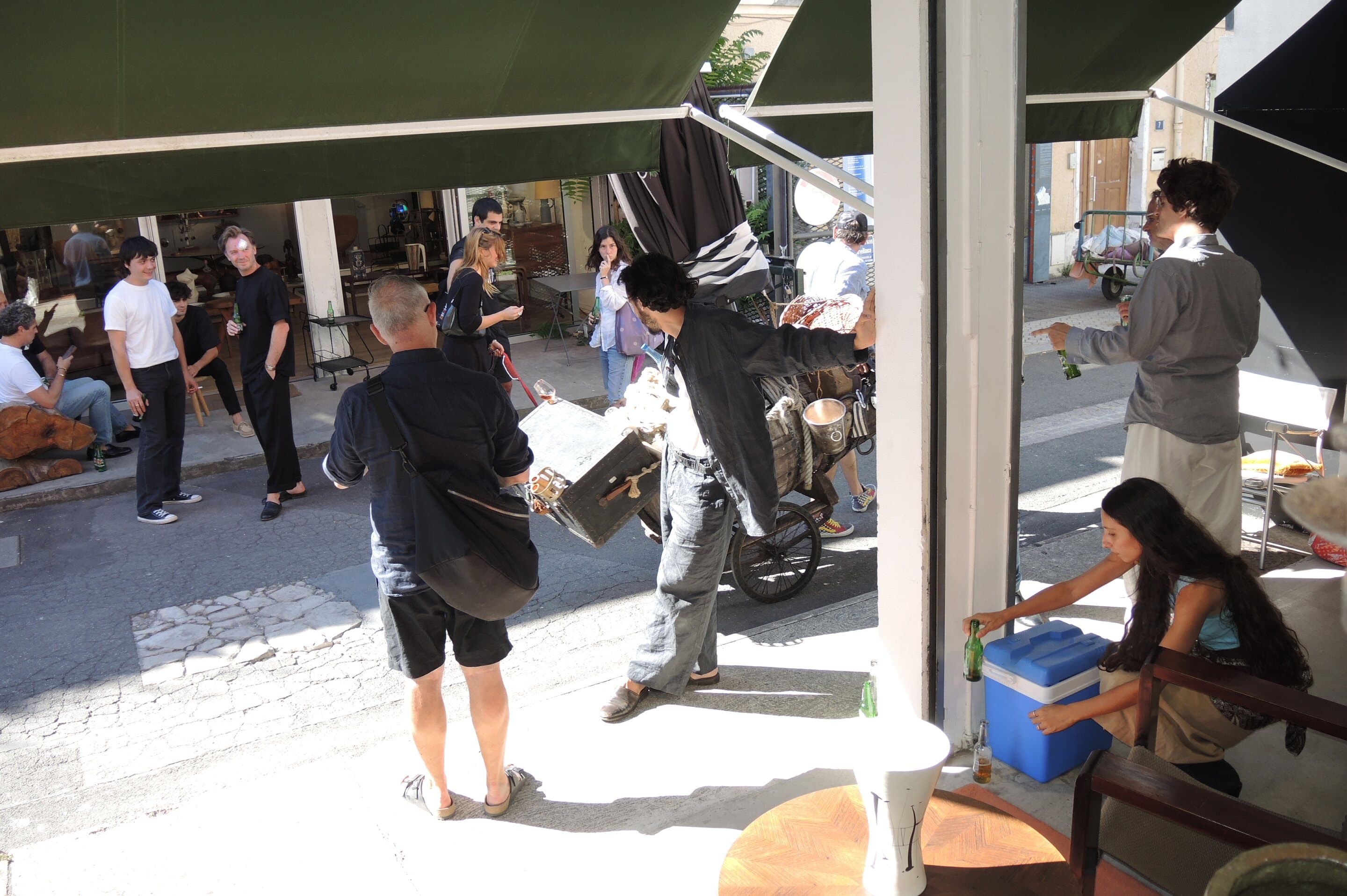 The alley outside the stand: passers-by, a scooter, a woman bent over a blue cool box