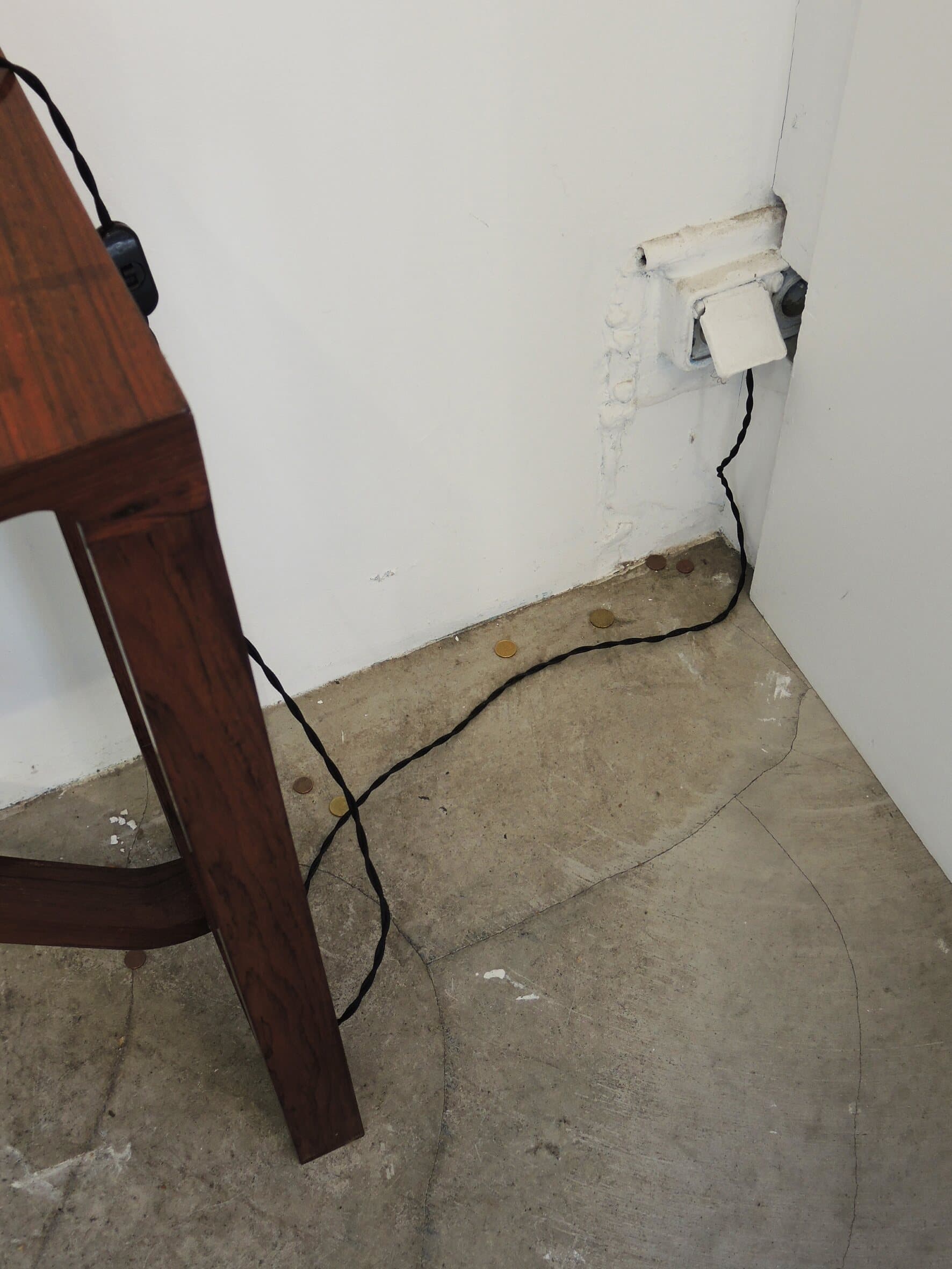 A corner of the stand: a table leg, a cable, a socket on the white wall