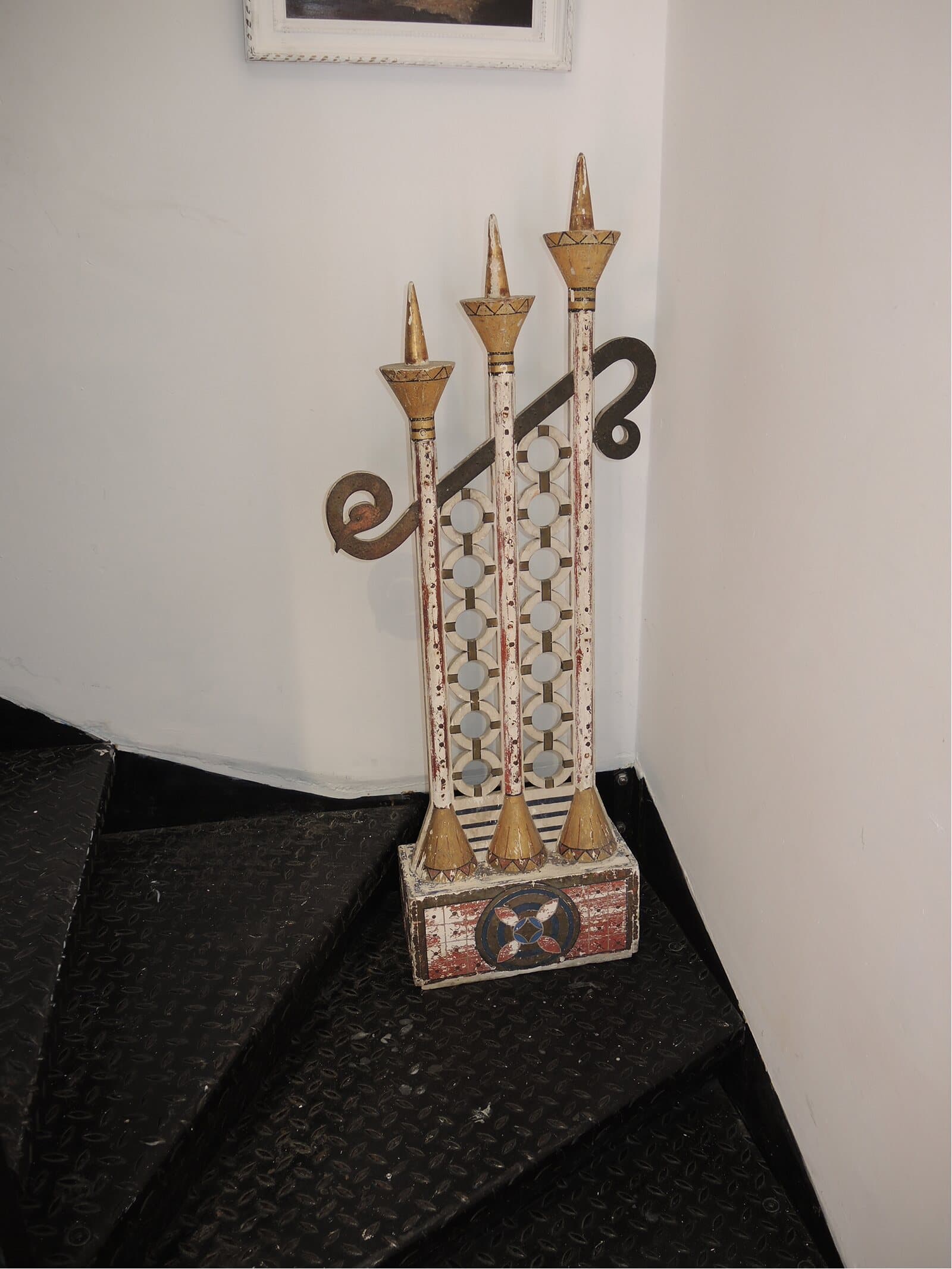 A painted wooden object with three gilded spires on a metal staircase