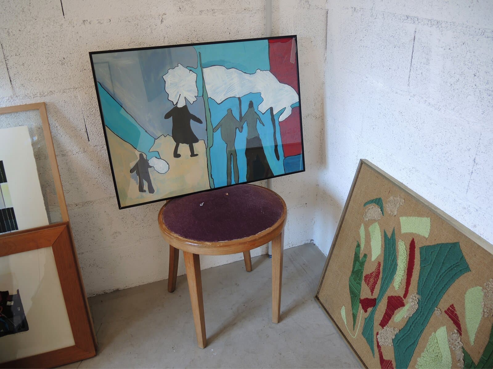 A stool in front of paintings leaning against a wall
