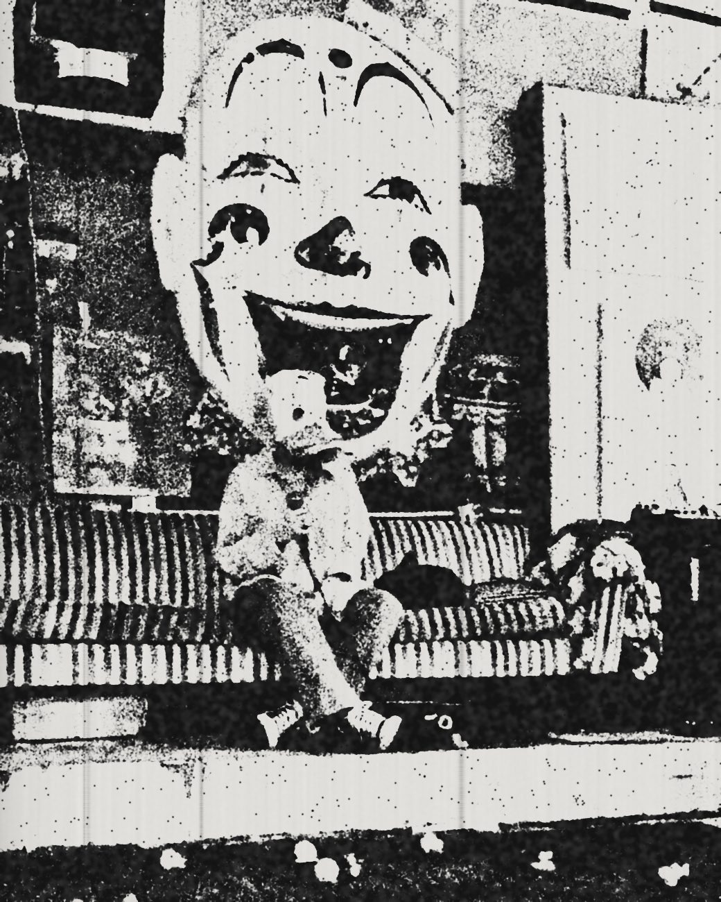 A performer in a duck mask on the striped couch under the giant clown face, as a photocopy